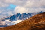 Dette bildet viser et majestetisk fjellandskap med bratte fjelltopper og en isbre som hviler i dalen