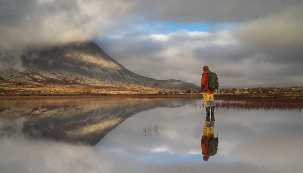 Mann i Døråla som nesten ser ut til å stå på vannet. Mannen og fjellet Stygghøi speiler seg i vannet. Høstssteming.